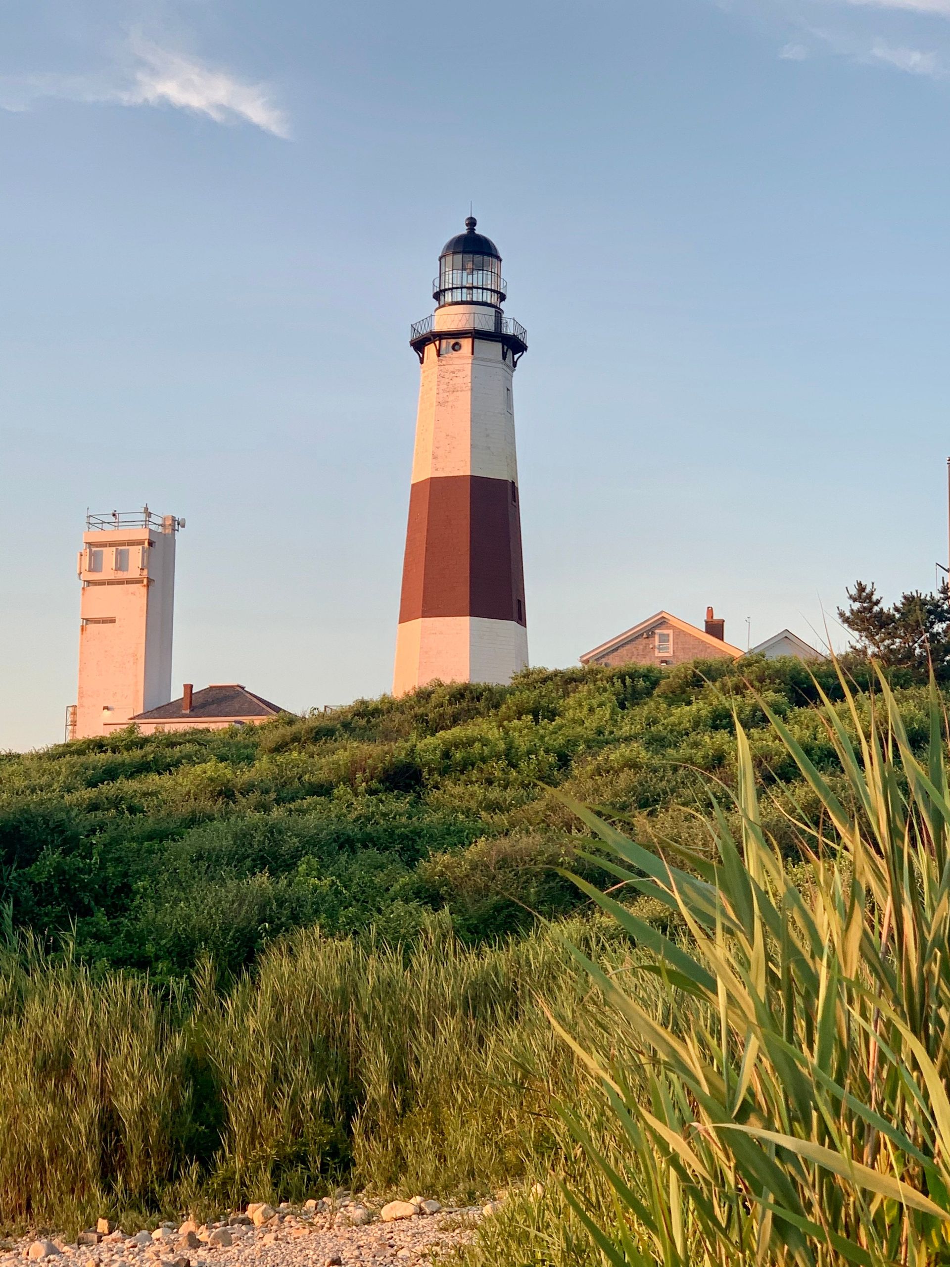 Scenic view of Montauk Point Lighthouse surrounded by lush greenery and summer sky.